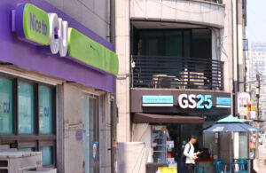 Утром человек заходит в корейский минимаркет, рядом магазины CU и GS25