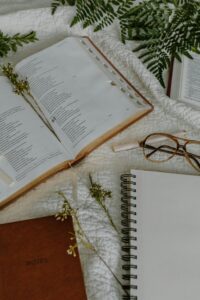 Открытая книга, тетрадь и очки лежат на столе