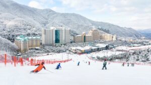 Лыжники спускаются по склону на курорте Вивальди парк в Корее, заснеженные горы и отели на фоне